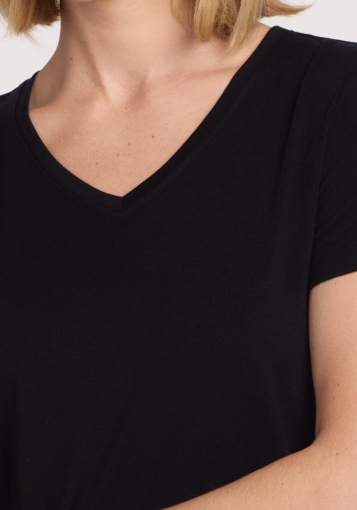 A close-up shows a person wearing the Woolx Junie V Neck - Black. Only the lower face, neck, shoulder, and upper chest are visible, with short blonde hair—highlighting this odor-resistant Merino wool essential.