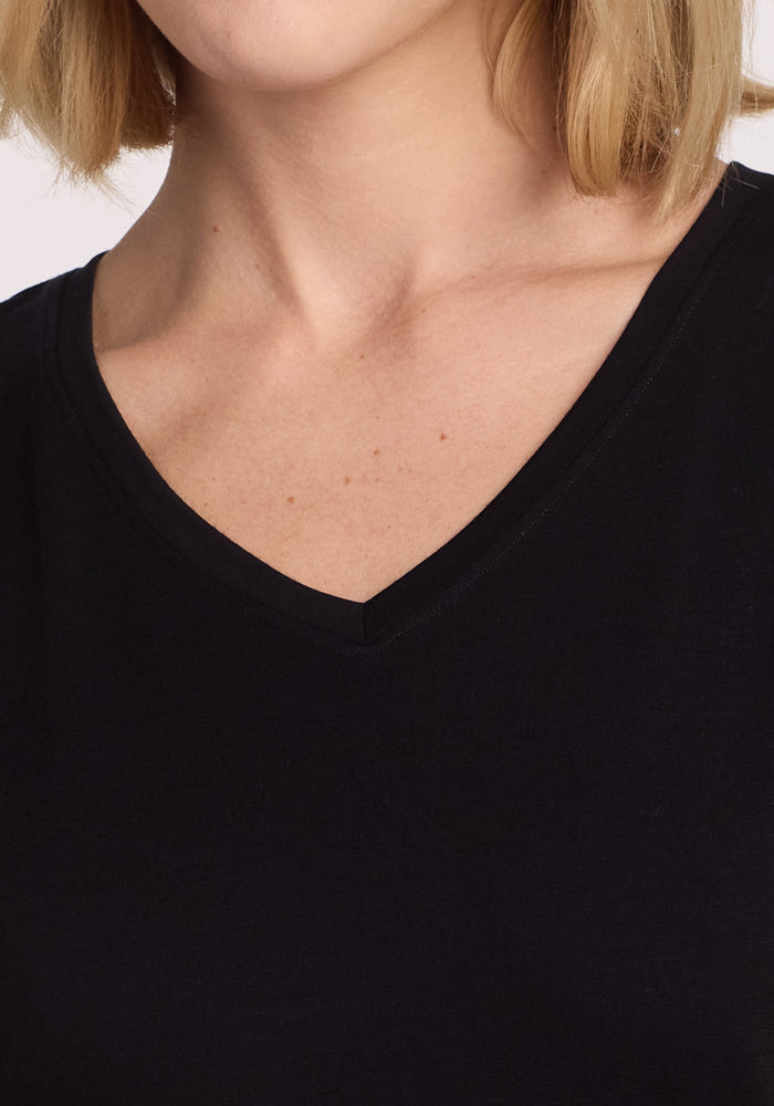 Close-up of a person wearing the Woolx Junie V Neck - Black, a women's relaxed fit Merino wool tee. Only the lower half of the face, neck, and upper chest are shown. The background is plain; the person has light skin and blonde hair.