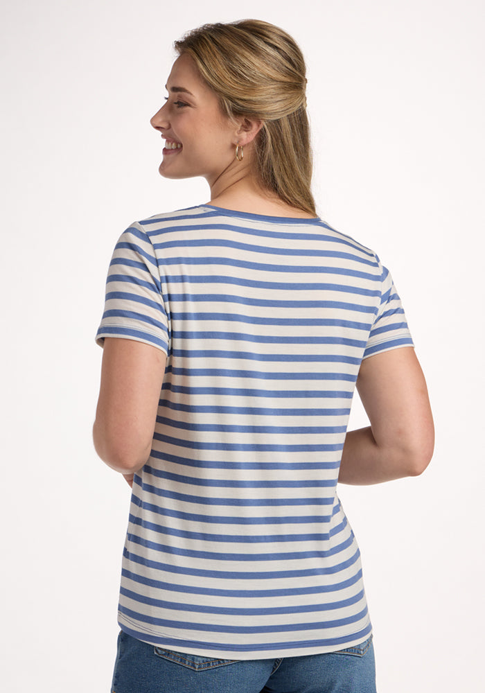A person stands facing away, smiling, wearing the Woolx Junie V Neck in Blue Sand Stripe with blue jeans, against a plain light background.