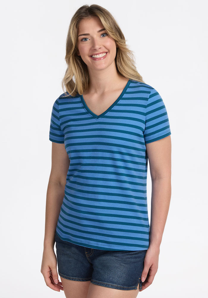 A smiling woman with long, wavy blonde hair wears the Woolx Junie V Neck - Coastal Stripe, paired with denim shorts, standing against a plain white background. | Ariana is 5'11", wearing a size S