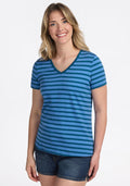 A smiling woman with long, wavy blonde hair wears the Woolx Junie V Neck - Coastal Stripe, paired with denim shorts, standing against a plain white background. | Ariana is 5'11", wearing a size S