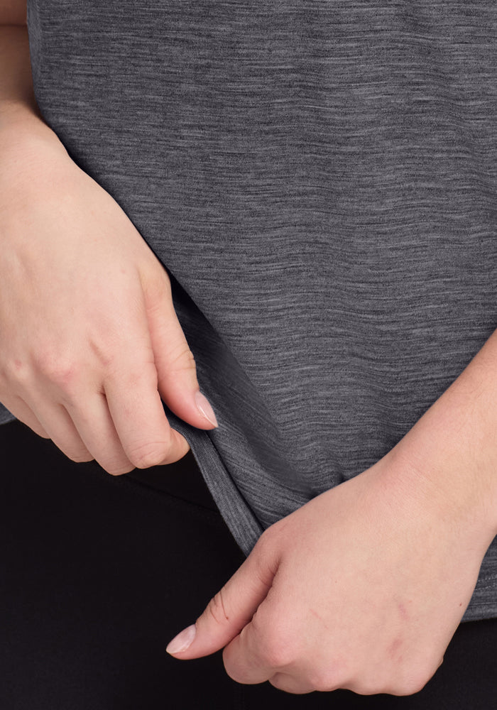 Close-up of hands gently tugging at the hem of the Woolx Junie V Neck in Cinder Melange, odor-resistant Merino.