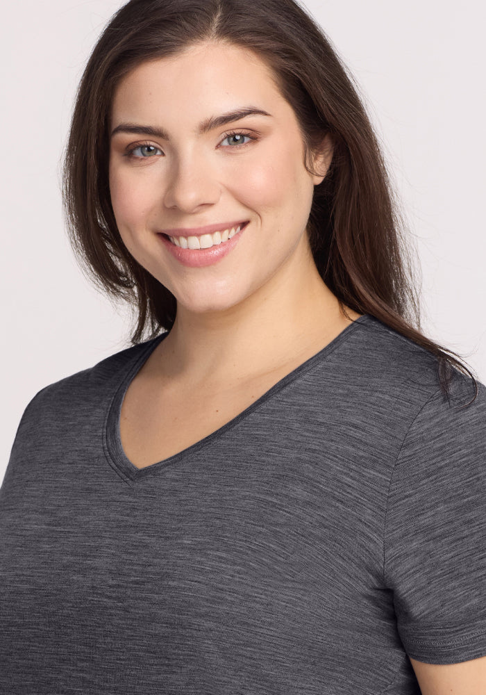 Smiling woman with long brown hair wears Woolx Junie V Neck in Cinder Melange, standing against a light background.