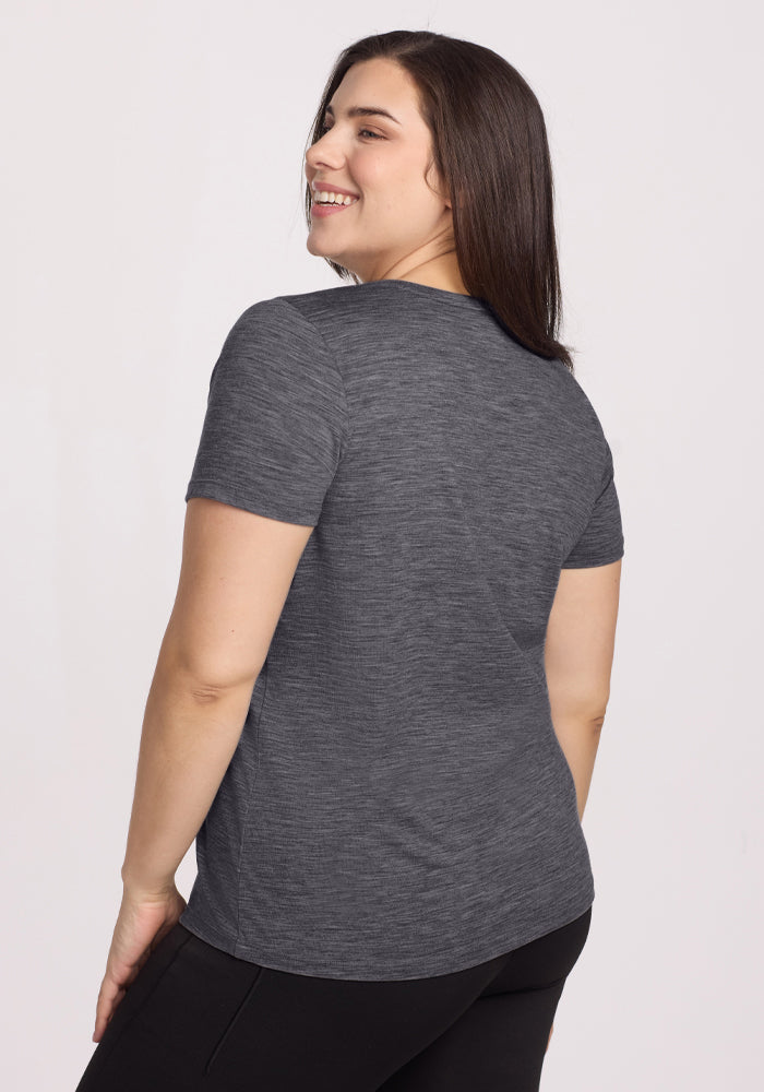 Woman with long dark hair smiles in the Woolx Junie V Neck tee in Cinder Melange and black pants, facing away.