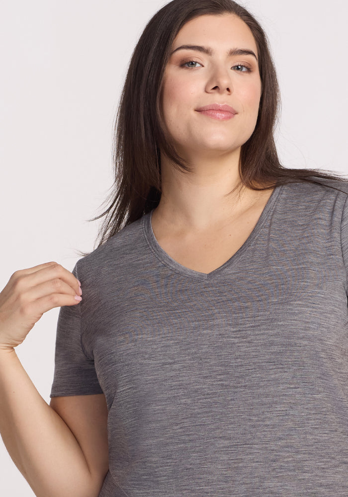 A woman with long brown hair smiles softly at the camera, wearing the Woolx Junie V Neck in Graphite Heather against a plain light background.