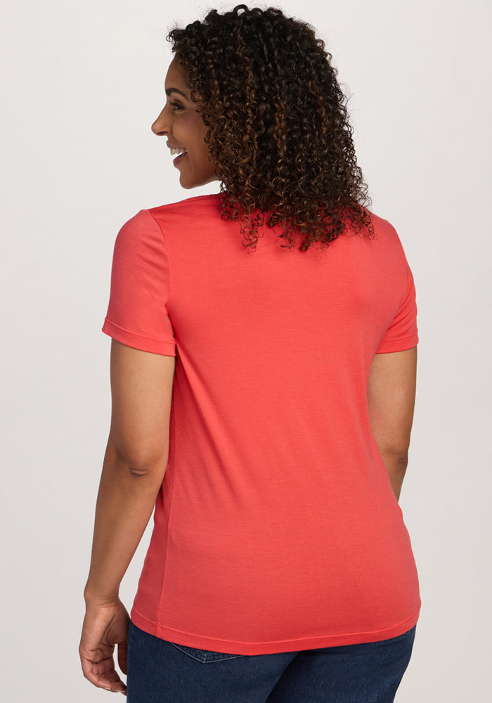 Smiling woman with curly hair in Woolx Junie V Neck - Hibiscus and jeans, facing away from the camera.