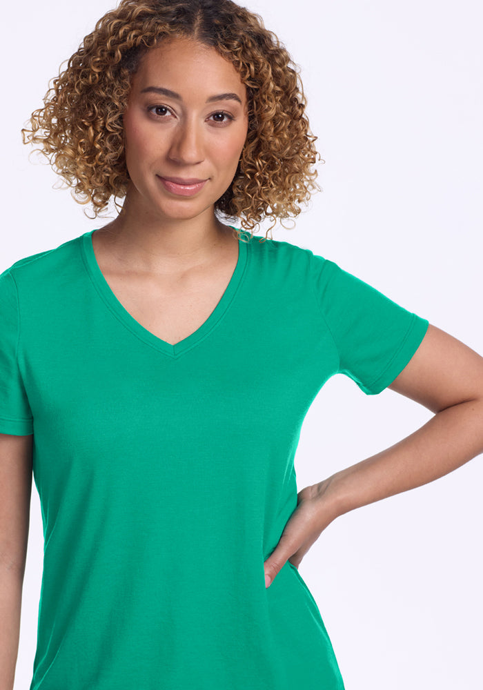 Smiling woman in the Woolx Junie V Neck - Jungle, relaxed fit, one hand on hip, against a light background.