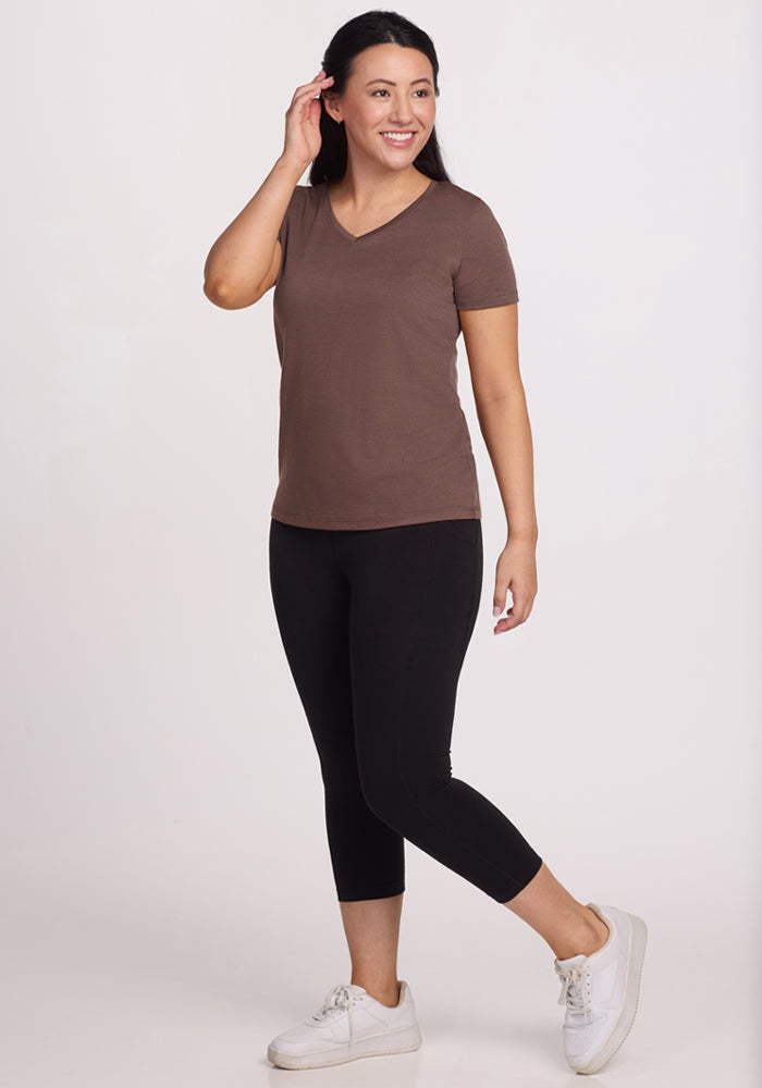 Woman in a Woolx Junie V Neck - Peppercorn, black leggings, and white sneakers, smiling against a plain background.
