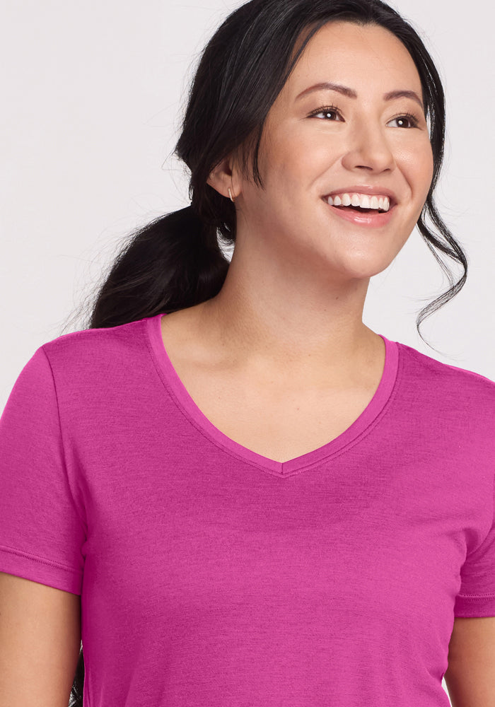 A smiling woman with long dark hair in a ponytail wears a bright pink Woolx Junie V Neck - Summer Sorbet tee.