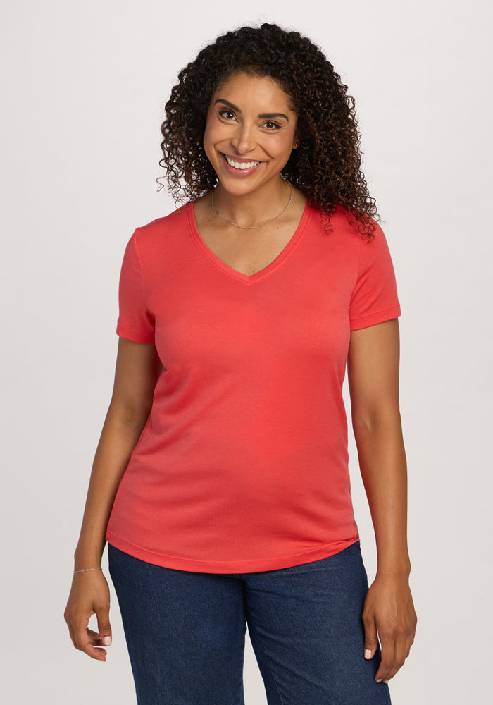 Smiling woman wears Woolx Junie V Neck - Hibiscus and blue jeans, standing against a plain light background. | Kisha is 5’8”, wearing a size M