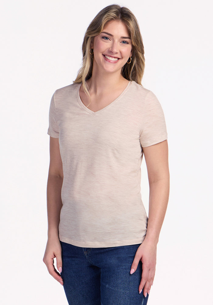 A smiling woman with long, light brown hair wears the Woolx Junie V Neck in Cream Heather and blue jeans, standing against a plain white background. | Ariana is 5'11", wearing a size S