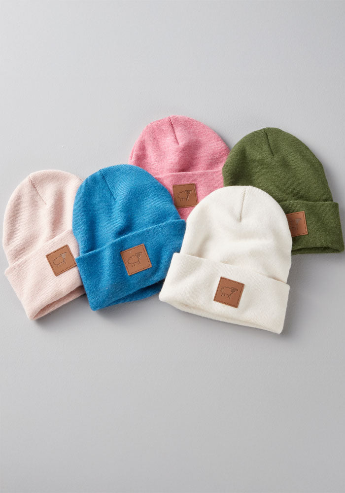 Five Woolx Kids Baylor Beanie - Whipped Cream hats are arranged on a gray background, in pastel colors—light pink, blue, pink, green, and white. Each wool beanie features a brown patch with an animal outline on the front.