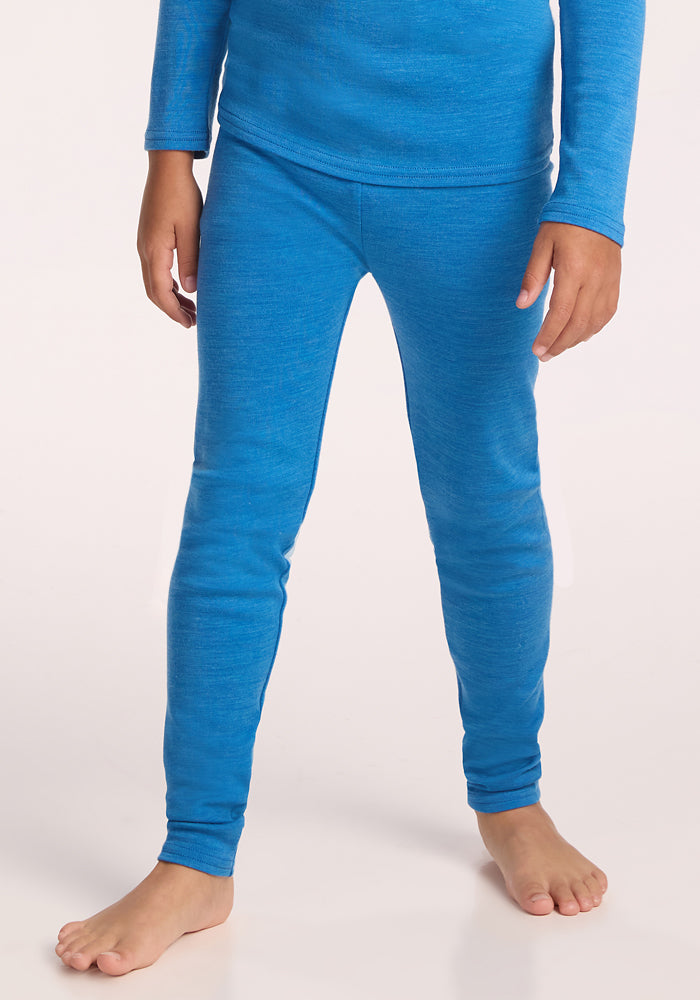 A child stands barefoot against a light background, shown from the neck down, wearing Woolx Kids Explorer Base Layer Bottoms in Blue Razz with a matching long-sleeve top. Only the body, arms, and legs are visible. | Rafael is wearing a size MED.