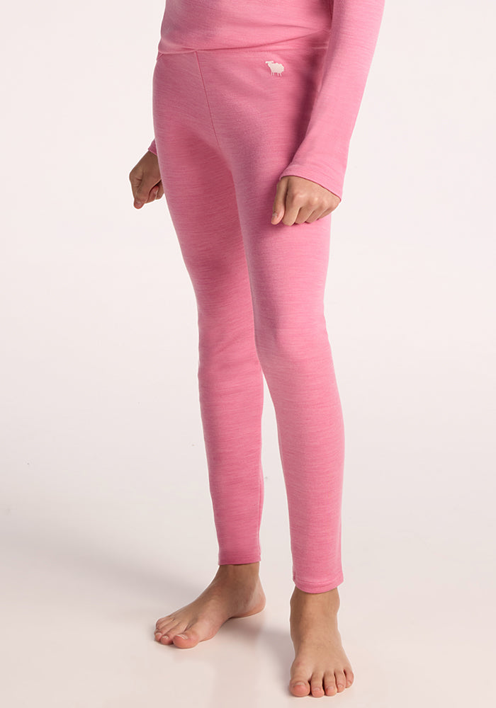 A child models Woolx Kids Explorer Base Layer Bottoms in Pinky Promise, barefoot against a plain light background. The warm merino wool leggings feature a small white animal logo near the hip. | Hanna is wearing a size LRG.