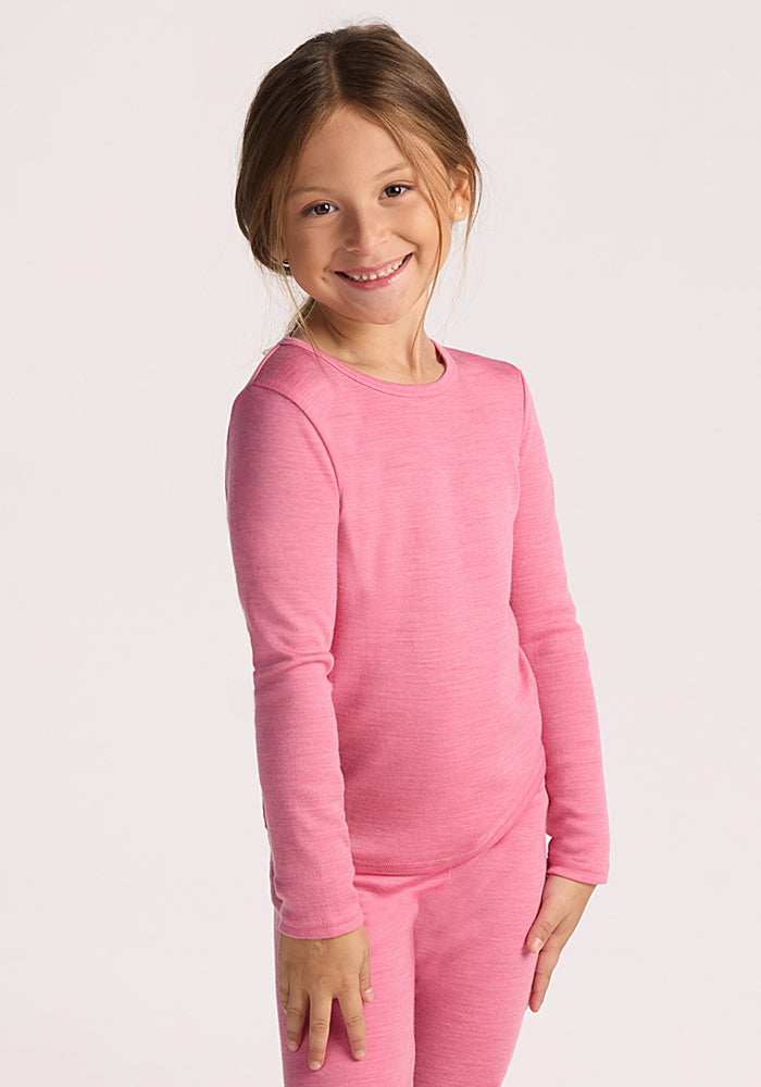 A young child with light brown hair smiles while wearing the Woolx Kids Explorer Base Layer Top - Pinky Promise, paired with matching pants, against a plain light background. | Aria is wearing a size XSM.