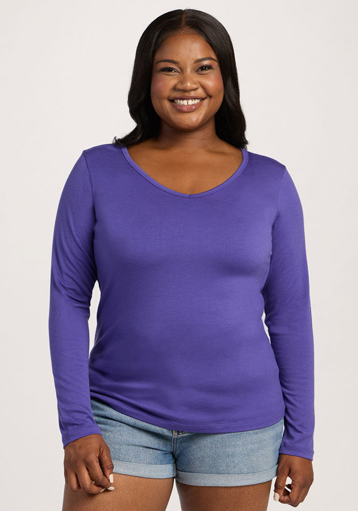 Smiling woman in a Woolx Layla V Neck Top - Berry Indigo and denim shorts stands against a light background. | Sapphire is 5’8”, wearing a size XL