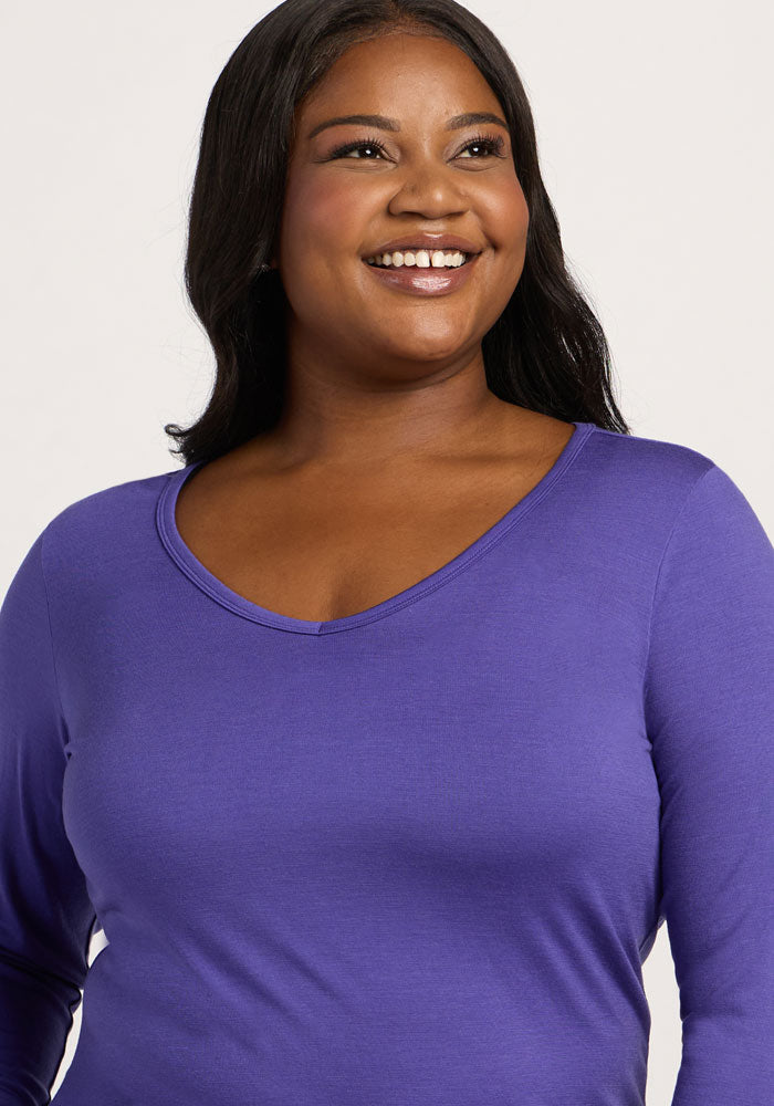 Smiling woman with long dark hair wears the Woolx Layla V Neck Top in Berry Indigo against a plain light background.