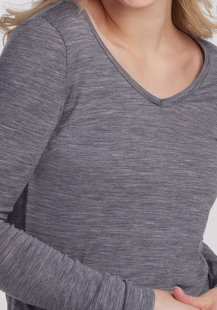 A person dons the Woolx Layla V Neck Top in Graphite Heather, made from moisture-wicking Merino wool. The neutral background highlights the top's sophisticated design and texture.