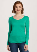 Woman with shoulder-length brown hair wears the Woolx Layla V Neck Top - Jungle and blue jeans, standing and smiling. | Shea is 5’9”, wearing a size S