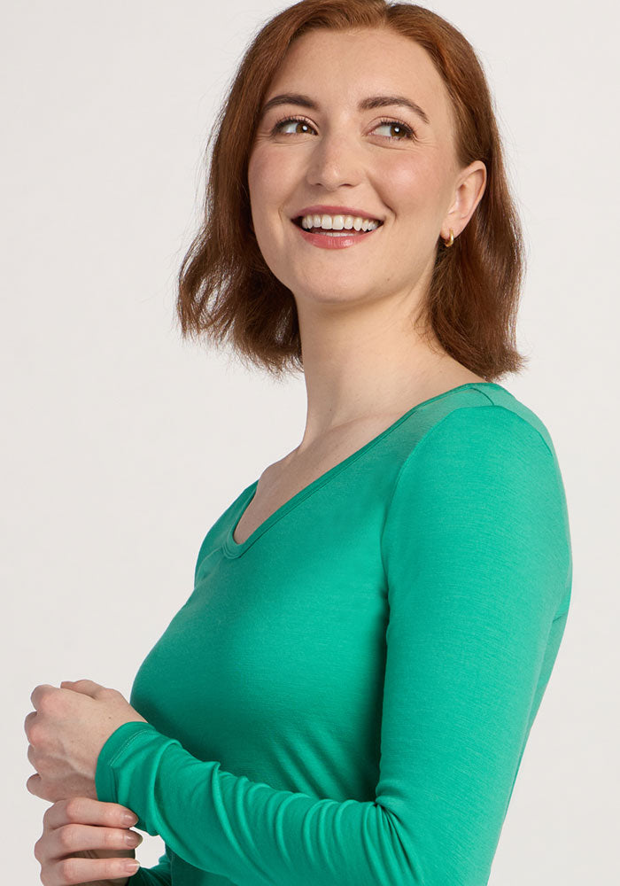 Smiling woman with short auburn hair wears the Woolx Layla V Neck Top - Jungle, looking to her left.