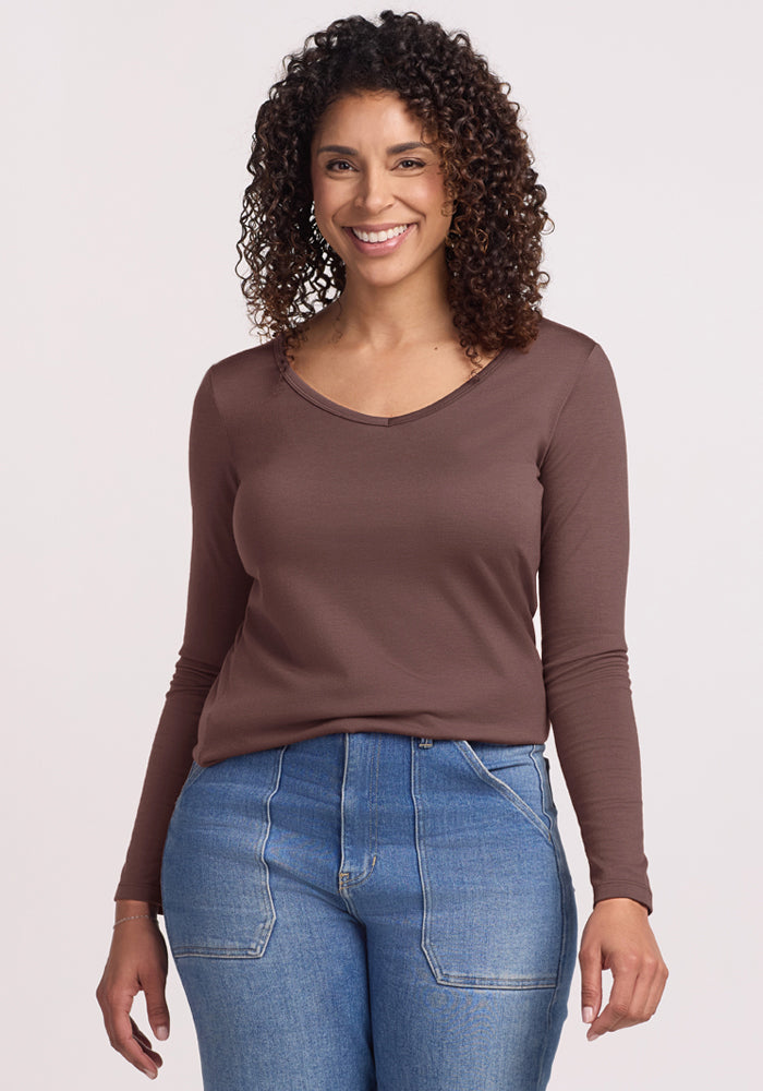 Smiling woman with curly hair wears the Woolx Layla V Neck Top in Peppercorn and blue jeans, against a light background. | Kisha is 5'8", wearing a size M