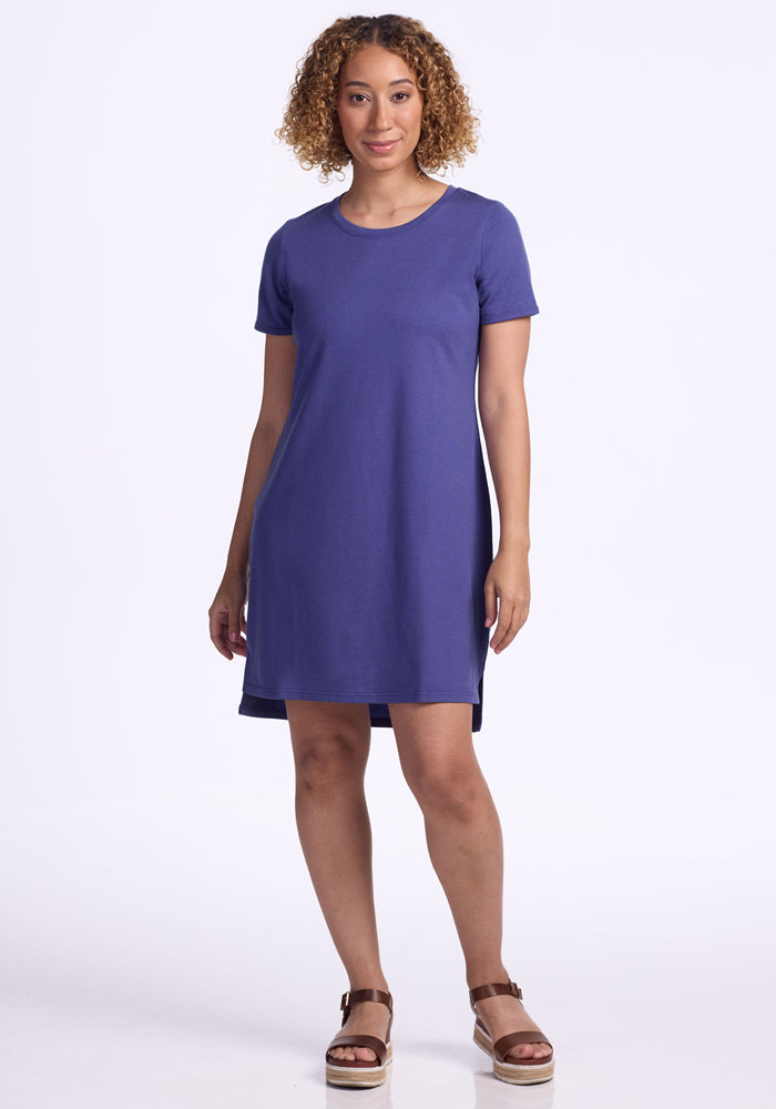 A woman with curly hair wears the Woolx Lexie Dress & Cover-up in Ink Blue, standing and smiling against a plain white background.