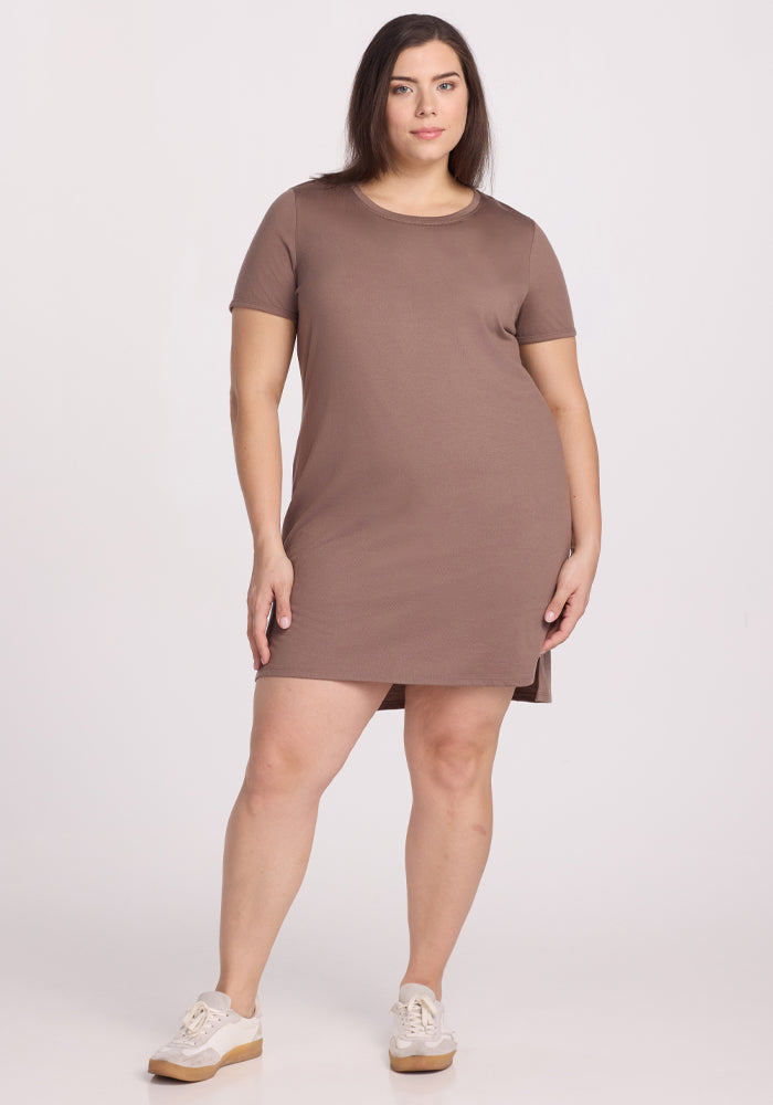 A woman with shoulder-length dark hair stands facing forward in a short-sleeve Woolx Lexie Dress & Cover-up in Toasted Almond, featuring a small side slit. She wears white sneakers against a plain white background. Final Sale Deals!.