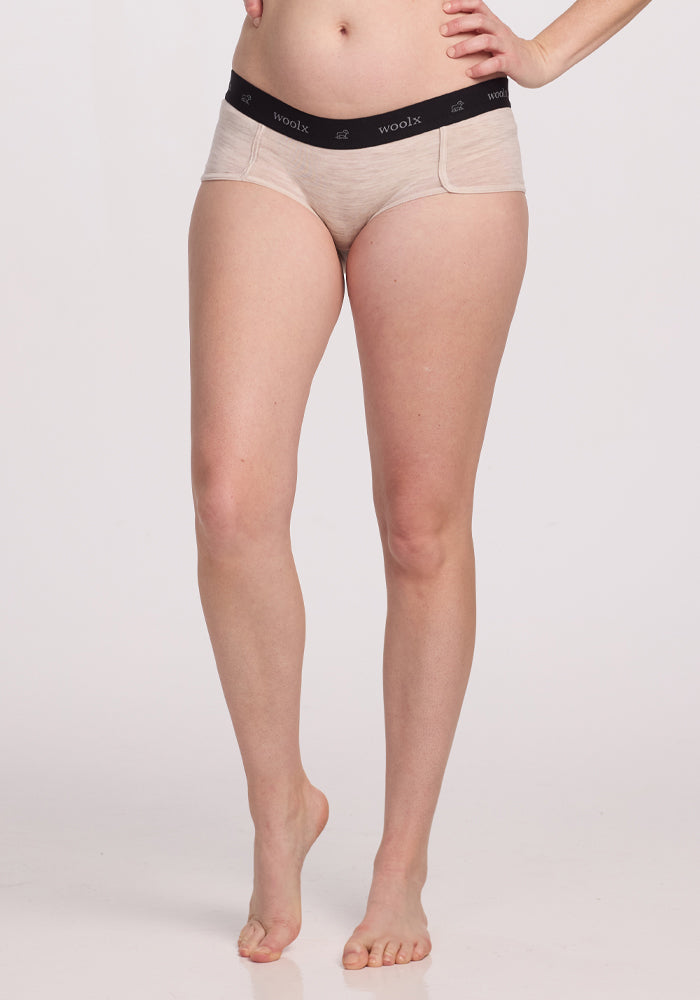 A person models the Woolx Lila Boy Shorts in Cream Heather, with a snug fit and black waistband for all-day comfort. One leg is bent, and arms are partially visible against a white background.