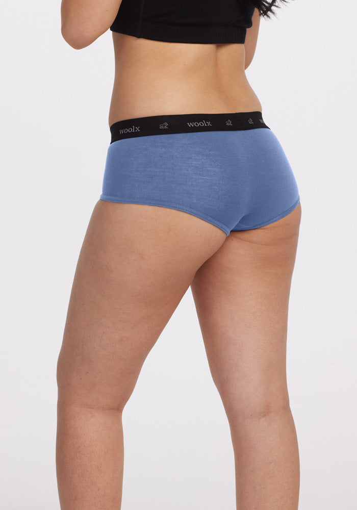A person is wearing Woolx's Lila Boy Shorts in Coronet Blue with a black waistband against a plain white background, highlighting the sporty construction that focuses on comfort at the lower back.