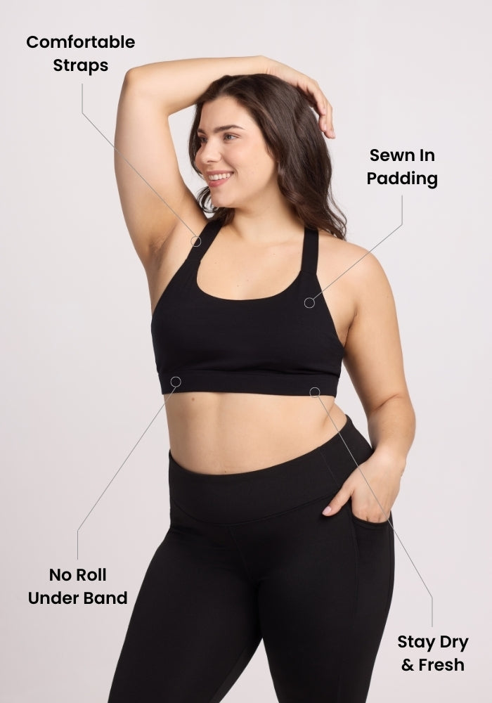 A woman in the Woolx Livi Bra - Cream Heather smiles with one arm raised. Labels highlight comfortable straps, sewn-in padding, a no-roll underband, and stay-dry & fresh fabric.