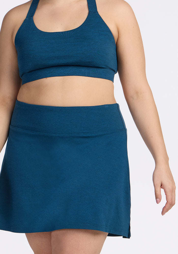 Woman wears Woolx Livi Bra in Majolica Blue with matching athletic skirt, shown shoulders to mid-thigh against a light background.