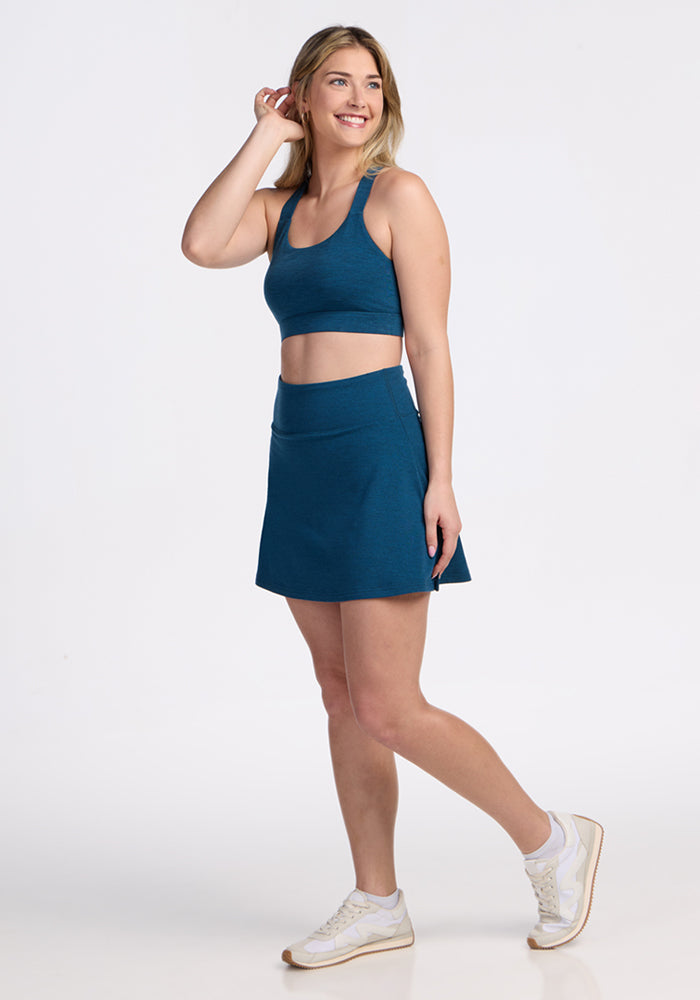 Woman in the Woolx Livi Bra • Final Sale - Majolica Blue, smiling and walking in white sneakers against a plain background.