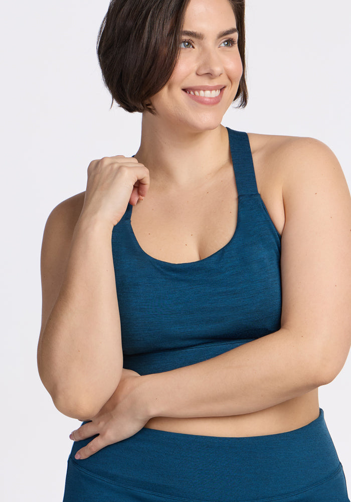 Woman with short brown hair smiles in the Woolx Livi Bra in Majolica Blue, arms crossed, looking to the side.