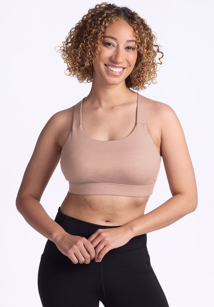 Woman with curly hair wears Woolx Livi Bra in Morning Latte, standing against a plain white background.