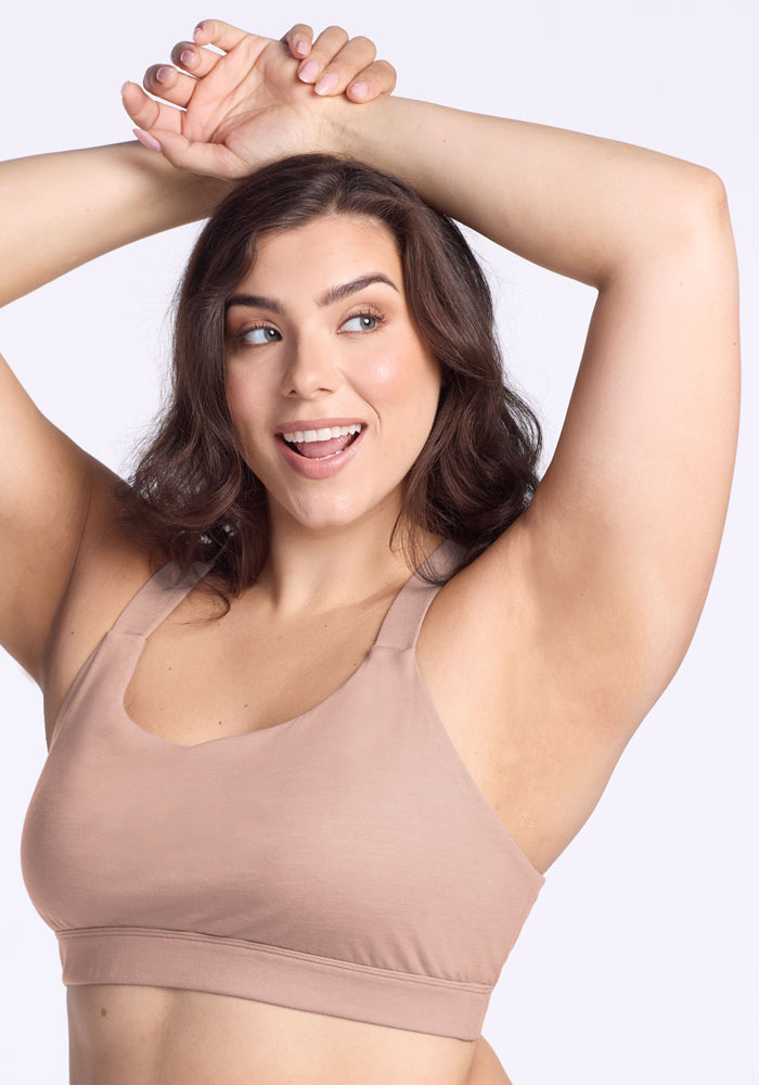 Smiling woman in Woolx Livi Bra • Final Sale - Morning Latte raises arms above head against a light background.