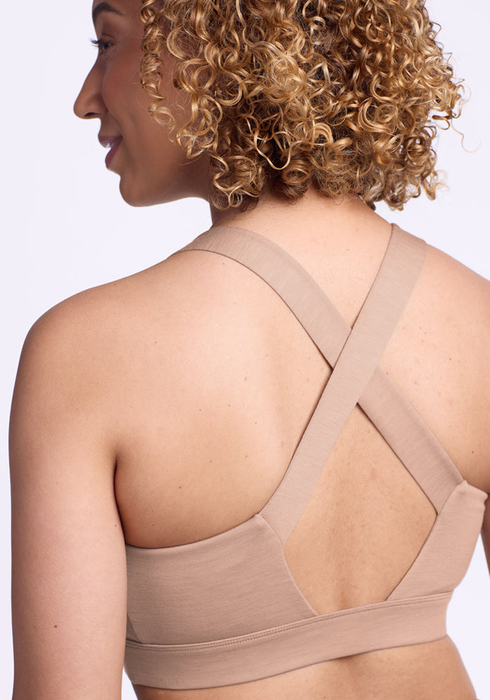 Woman with curly hair models the Woolx Livi Bra in Morning Latte, shown from behind against a light background.