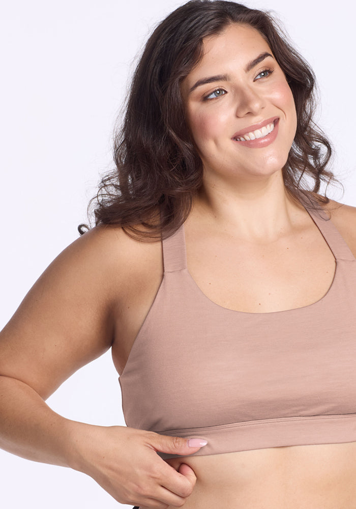 Smiling woman with long brown hair wears Woolx Livi Bra • Final Sale - Morning Latte, adjusting the hem with her left hand.