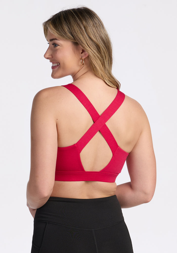 Woman wearing Woolx Livi Bra in Poppy Spark with crisscross straps and black leggings, shown from the back.
