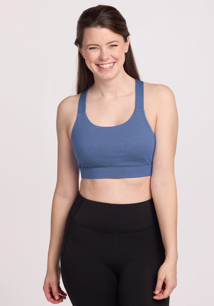Smiling woman wears the Woolx Livi Bra • Final Sale - Skyline, styled with black leggings against a light background.