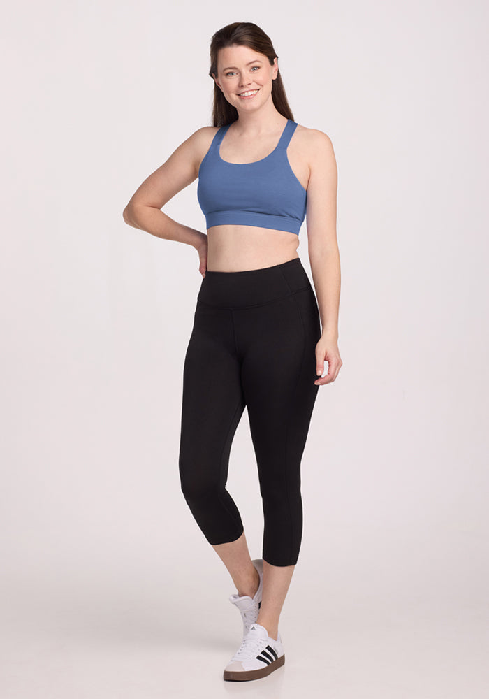 Woman in the Woolx Livi Bra • Final Sale - Skyline, black leggings, and sneakers smiles against a plain light background.
