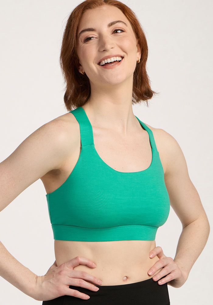 Smiling person with short red hair wears the Woolx Livi Bra - Jungle and black pants against a plain light background.