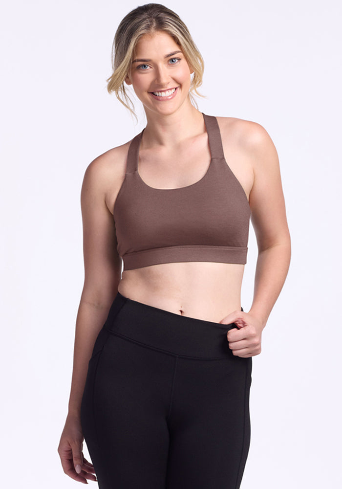 Woman smiles in Woolx Livi Bra - Peppercorn and black leggings against a plain light background. | Ariana is 5'11", wearing a size S