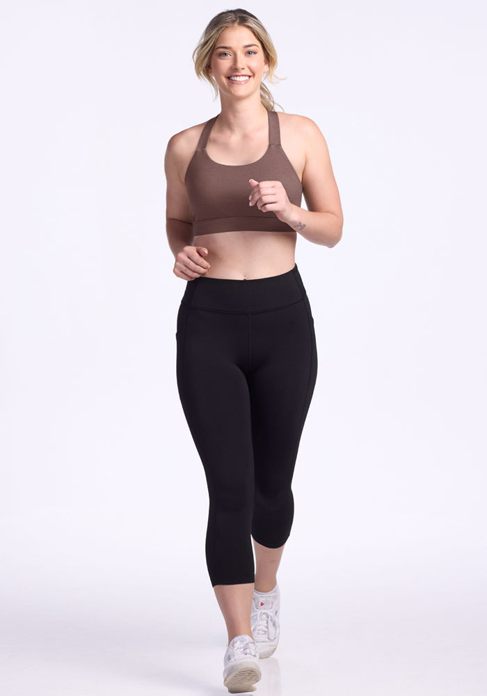 Woman jogging and smiling in Woolx Livi Bra - Peppercorn and black leggings on a plain white background.