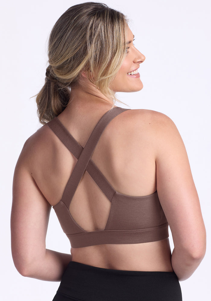 Woman smiling in the Woolx Livi Bra - Peppercorn with crisscross straps and black leggings against a light background.