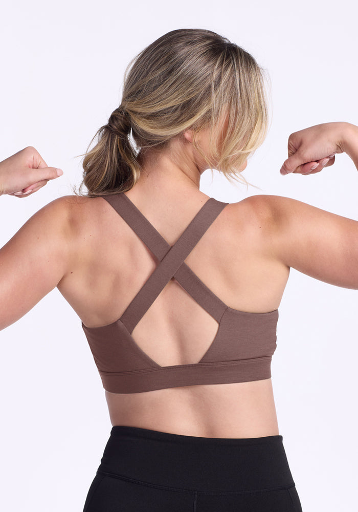 Blonde woman in ponytail flexes, wearing Woolx Livi Bra - Peppercorn and black leggings.