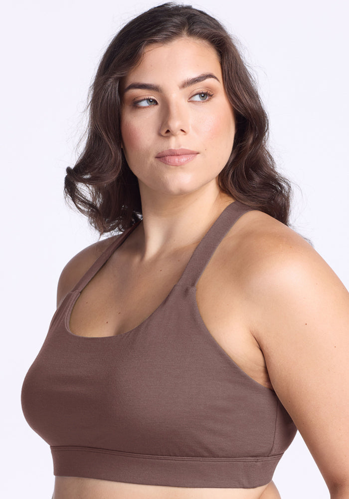 A woman with wavy brown hair models the Woolx Livi Bra in Peppercorn, looking to the side against a light background.