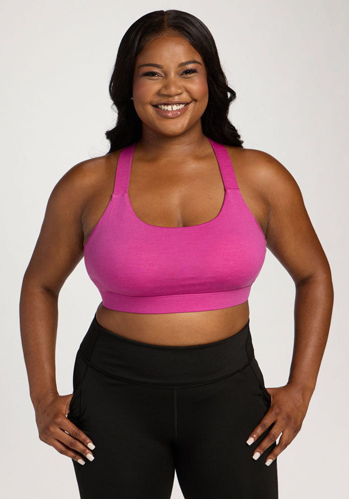 Smiling woman wears Woolx Livi Bra - Summer Sorbet and black leggings, standing with hands on hips against plain background. | Sapphire is 5’8”, wearing a size XL