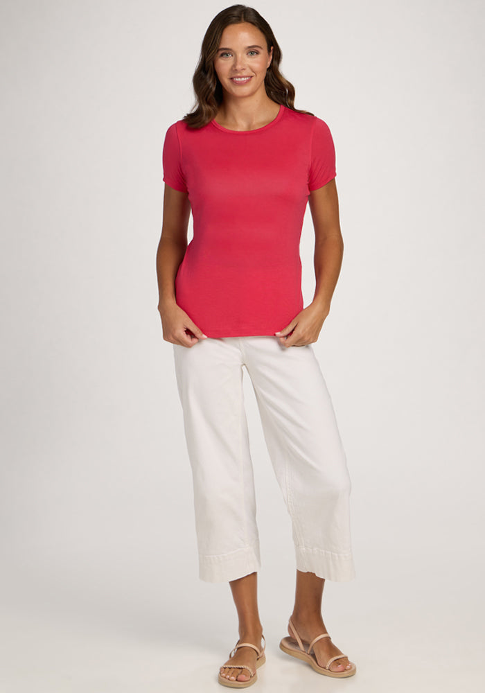 Woman wearing the Woolx Liza Crew Neck Tee in Berry Ice Pop, white pants, and sandals, smiling against a light background.