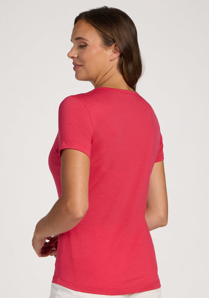 Woman wearing Woolx Liza Crew Neck Tee in Berry Ice Pop and white pants, standing, looking over her shoulder.