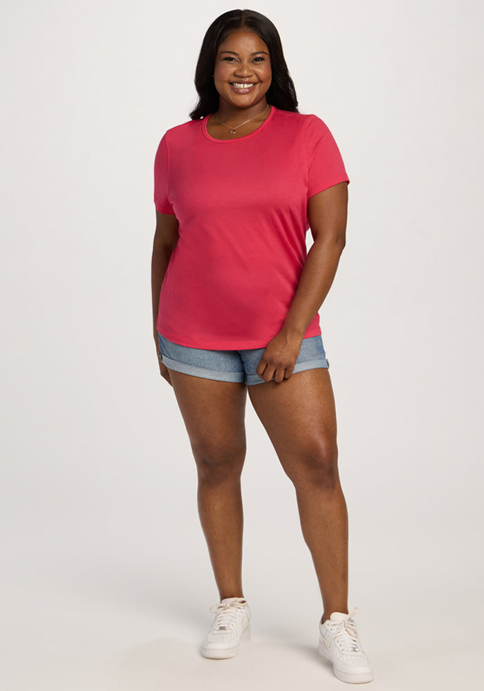 Woman smiling, wearing the Woolx Liza Crew Neck Tee in Berry Ice Pop with denim shorts and white sneakers.